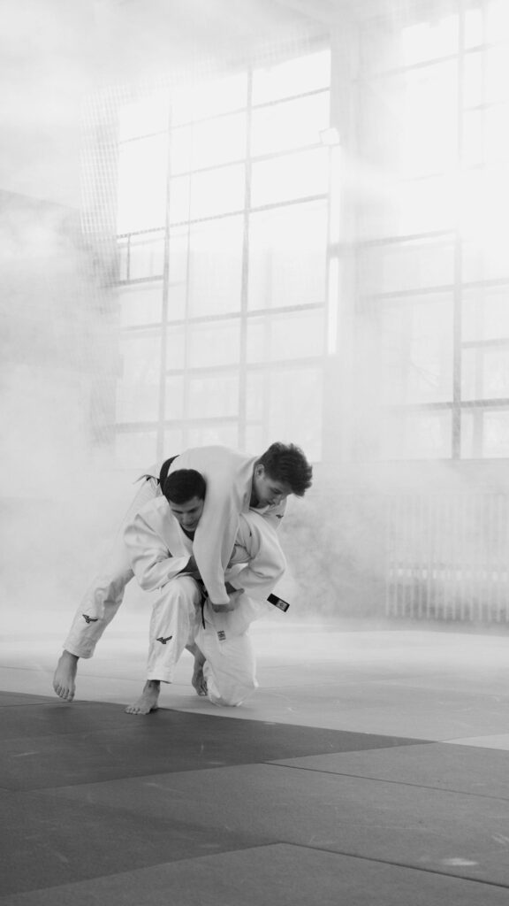 Two martial artists practicing judo indoors, captured in a monochrome setting.